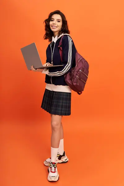 A young woman in a trendy outfit holds a laptop, showcasing a confident pose in a studio. — Stock Photo