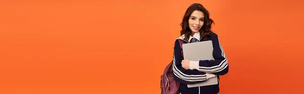 A cheerful young woman poses confidently with her laptop and bag against an orange backdrop, banner — Stock Photo