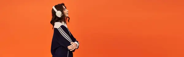 A young woman in a jacket listening music against a bright orange backdrop, banner — Stock Photo