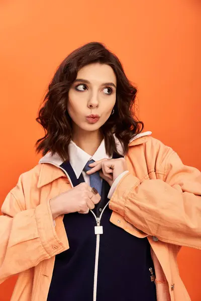 A young woman showcases her modern fashion sense with confidence against an orange backdrop. — Stock Photo