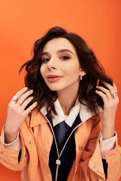 A young woman in a trendy outfit poses confidently against a bright orange backdrop. — Stock Photo