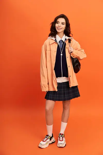 A young woman showcases her fashionable skirt and jacket on a bright orange backdrop in a studio. — Stock Photo