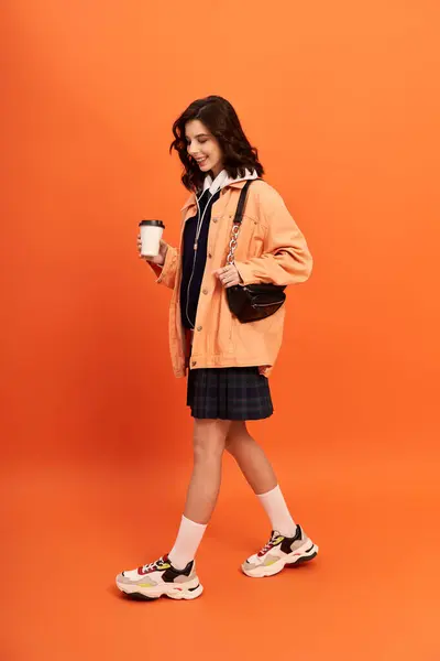 A young woman walks confidently in a fashionable outfit, exuding style in an orange studio. — Stock Photo