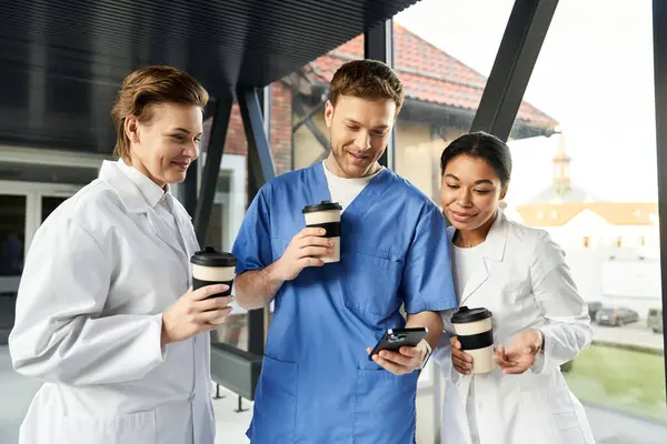Three multicultural medical professionals enjoy coffee while discussing a case in the hospital. — Stock Photo