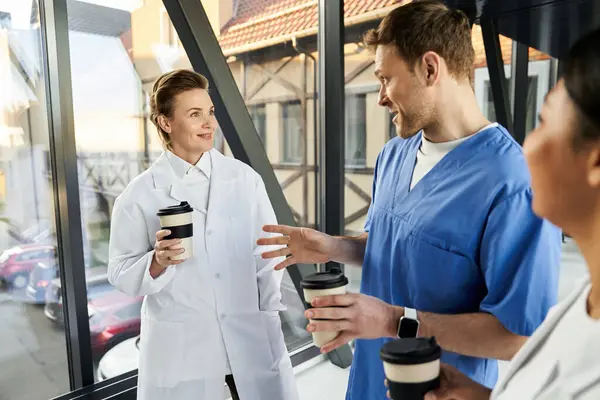 Multicultural medical staff share insights while enjoying coffee in a hospital corridor. — Stockfoto