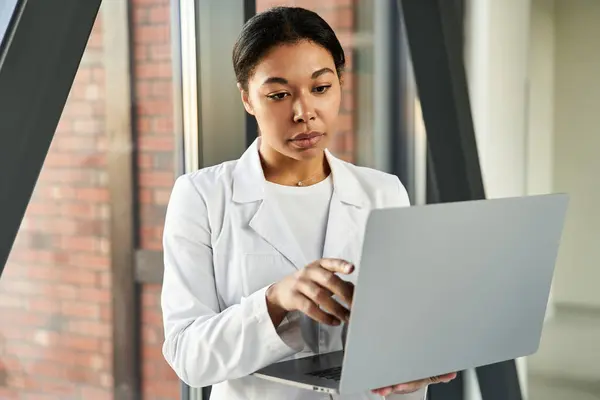 African american doctor in white coat using her laptop to deliver quality healthcare. — стокове фото