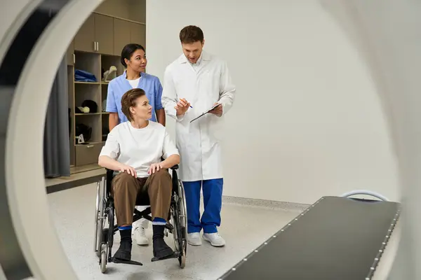 Handsome doctor and nurse prepare female patient in wheelchair for MRI scan in modern facility. — Stock Photo
