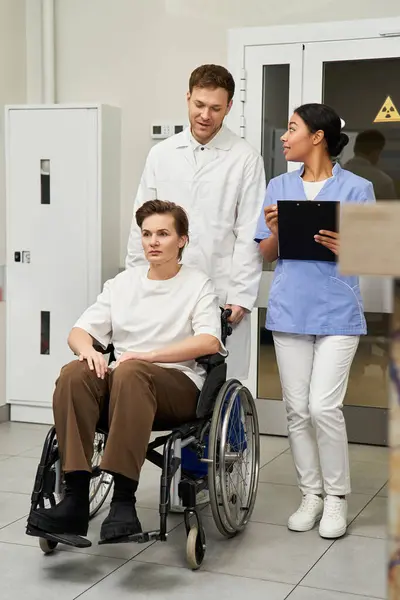 Handsome doctor and nurse support a female patient in a wheelchair before MRI scan. — Stock Photo