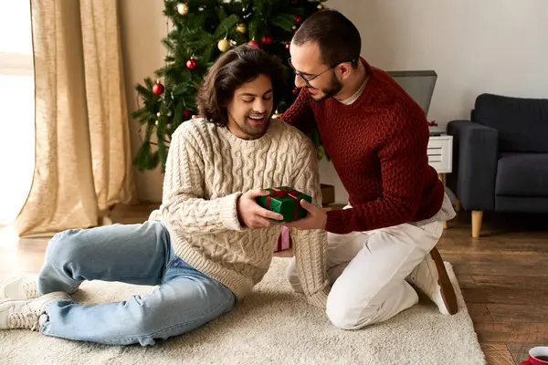 Двое мужчин обмениваются красиво обернутым подарком в уютной гостиной, наполненной праздничными радостями. — стоковое фото