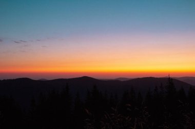 Ormanda gün batımı olan bir dağın silueti.