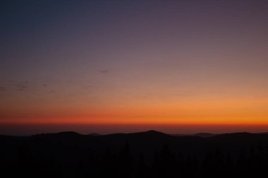 Ormanda gün batımı olan bir dağın silueti.