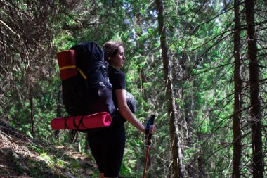 Sırt çantalı bir kadın ormanda dağlarda yürüyor.