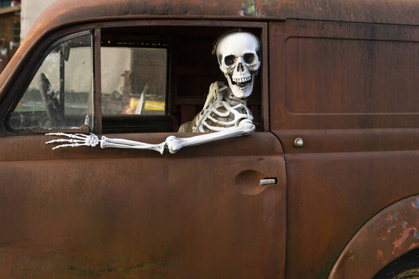 Человеческий скелет, сидящий в старой ржавой машине и смотрящий в окно
