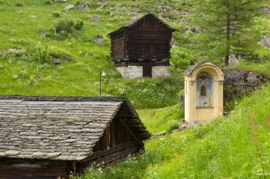 Switzerland, Bosco Gurin, 18. June 21. Historic holy shrine with colorful painting and wooden houses clipart