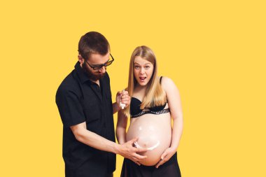 Adam hamile bir kızın karnına kremalı gülen surat çiziyor..