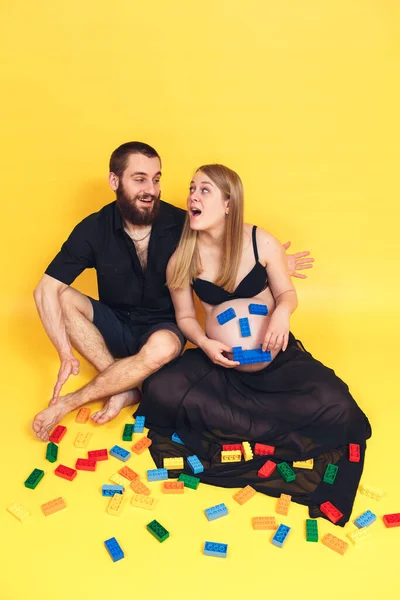 A pregnant couple plays with a constructor. Emoji from the constructor on the stomach.