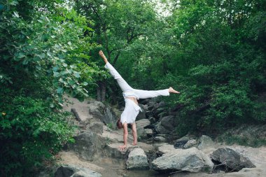 a young guy is doing yoga in nature, performing a handstand