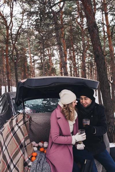 Picnic in the winter in the car. The couple kiss and drink tea from a thermos