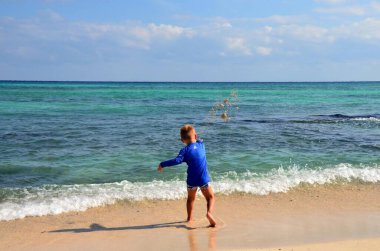 Bir yaz günü Karayip Denizi 'nin kıyısında duran bir çocuk, denize avuç dolusu kumla oynuyor.