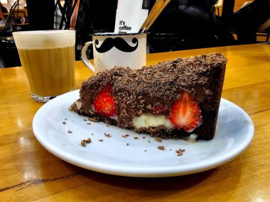 Kahve dükkanının masasında krema ve çilekle dolu sütlü kahve ve çikolatalı kek.