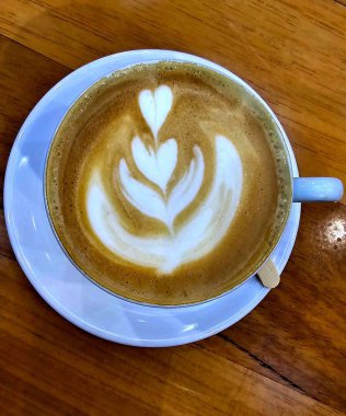 Beyaz bir fincan, beyaz bir fincan, ahşap bir masanın üzerinde, içinde kapuçino ve süt köpüğünden yapılmış kalpler