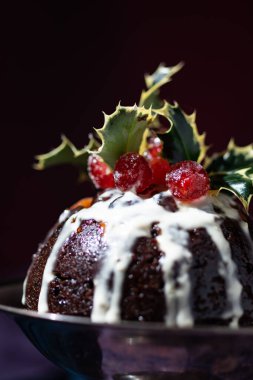 Geleneksel Noel meyveli puding tatlısı, kiraz ve yapraklarla süslenmiş, klasik kırmızı, mavi ve mor arka planda.