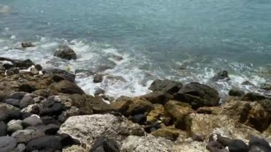 Yumuşak Dalgalı Rocky Shore. Güneşli bir günde sakin dalgaların yavaşça kayalara çarptığı kayalık bir kıyı şeridi..
