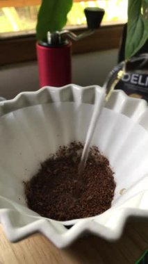 Filtredeki kahve öğütülerinin üzerine su dökülüyor. El yapımı demleme için beyaz filtrede taze öğütülmüş kahvenin üzerine su döken yakın plan..