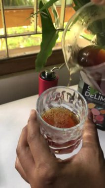 Taze demlenmiş kahveyi bardağa dolduruyorum. Cam sunucudan desenli cam bir fincana kahve döken bir elin yakın çekimi..