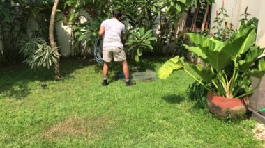 Elinde hortumla çimlerin üzerinde duran bir adam var. Adam elinde hortumla çimlerin üzerinde duruyor. Bahçe, peyzaj, açık hava aktiviteleri, yaz konseptleri, su koruma ve çevre temaları için elverişli.