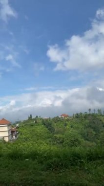 Bereketli Tropikal Manzaranın Ortasındaki Tepe Köyü. Parlak mavi bir gökyüzünün altında canlı yeşilliklerle kaplanmış, yuvarlanan tepelerin arasına kurulmuş sakin bir köy..