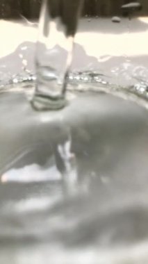 Su akıntısı yüzeye çarpıyor. Bir su akıntısına yakın çekim, yüzeye çarpar, kabarcıklar ve kabarcıklar yaratır..