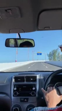 Coastal Road Trip Sürücü Perspektifi. Mavi gökyüzü ve uzak bir köprüsü olan kıyı otoyolu boyunca araba sürerken pov çekimi.