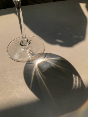 Bir şarap kadehi beyaz bir yüzeye gölge düşürür. Güneş ışığı camı kırarak renkli desenler oluşturur..