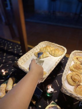 Bir el, çeşitli hamur işleriyle dolu bir sepetten kruvasan almak için dernek kullanır.