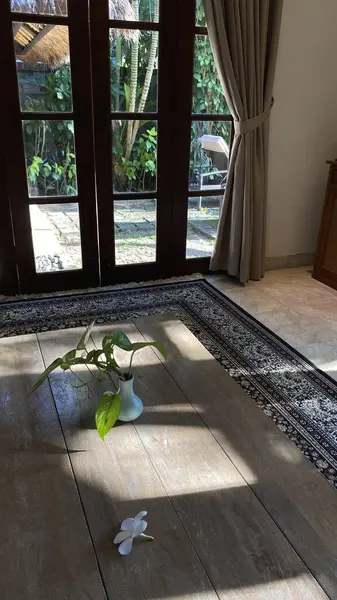 Açık Fransız kapılarını çerçeveleyen bej perdeli güneşli bir oda, yemyeşil bir bahçe ve yüzme havuzu manzarası ortaya çıkarıyor..