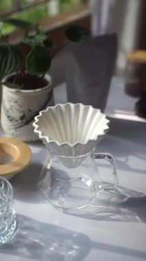 YOGYAKARTA, INDONESIA - 16 EPTEMBER 2023: Bir kişi seramik bir V60 damlatıcısını cam sunucuya yerleştirerek ve kağıt filtresini bir kaz boynundan gelen sıcak suyla durulayarak kahve yapmaya hazırlanıyor 