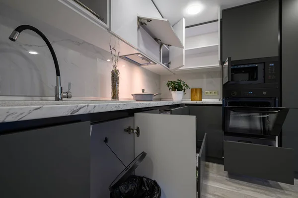 Showcase interior of modern simple dark grey and white kitchen, drawers retracted, doors open
