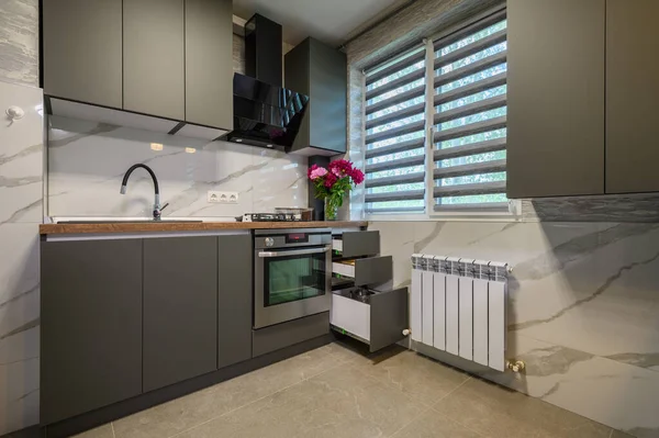 Real showcase interior of small modern trendy gray kitchen, drawrs retracted to show inside