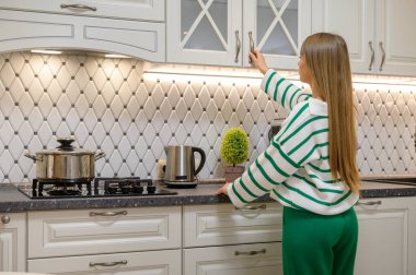 Tatlı, genç, uzun saçlı ev hanımı mutfak dolabının kapısını açıyor.