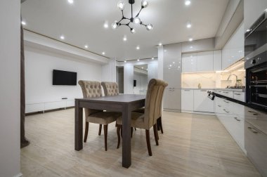 Duvarında televizyon olan büyük, beyaz, lüks bir stüdyo daire, büyük bir mutfak, bir sürü fotokopi alanı, sandalyeli yemek masasına yakın görüş.