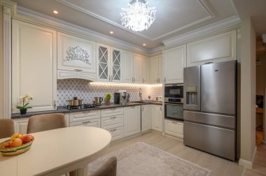 Bej renkli ve klasik tasarım unsurları olan şık, açık fikirli bir mutfak. Meyveli yemek masasına yakın.