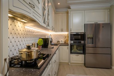 Bej renk şeması ve klasik tasarım unsurları olan şık, açık konsept bir mutfak.