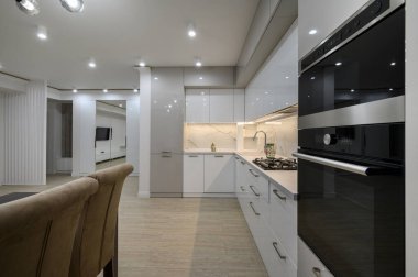 Duvarında televizyon olan büyük, beyaz, lüks bir stüdyo dairenin içinde büyük bir mutfak, bir sürü fotokopi alanı, sandalyeli yemek masasının yakın görüntüsü.