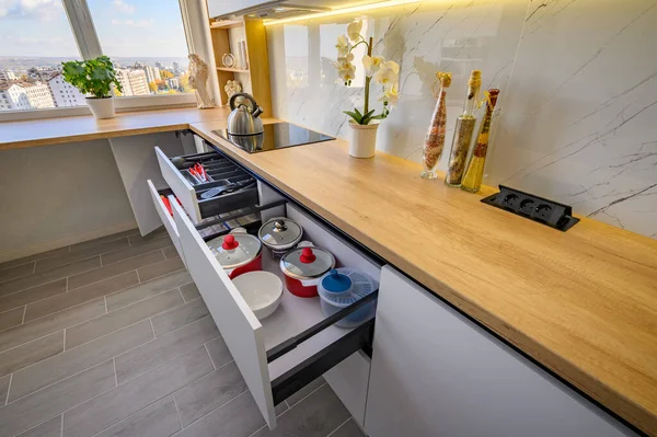 A sleek white kitchen with drawers extended to reveal their contents, high angle view