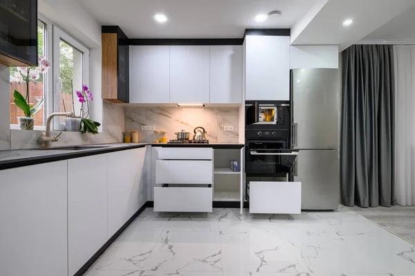 A functional and stylish kitchen with a white design, a marble floor, an open oven door, and pull-out shelves for convenient storage and organization