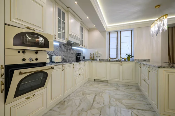 Closeup of classic cream-colored kitchen with appliances including oven, microwave, and coffee maker, oven door is open