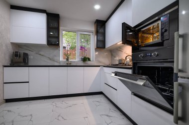 Pürüzsüz, modern aletlerle yenilenmiş bir mutfak, mermer zemin ve modern kapaklar, fırın ve mikrodalga fırın açık.