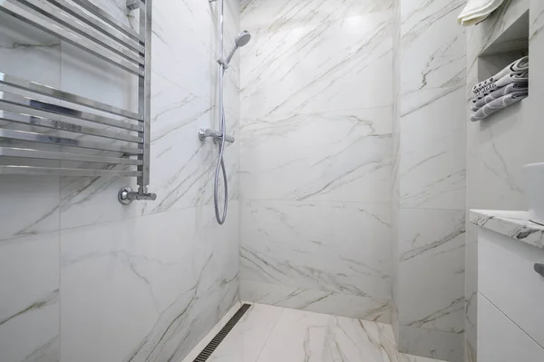 White bathroom interior with marble tiles on the walls and shower