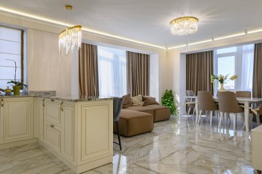 Classic kitchen in creamy color with a spacious and bright design, island, and dining area in a studio apartment with a brown sofa and pillows